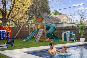 A backyard with a wooden playhouse, a slide, and a swimming pool. - Gated Heated Pool - Large Playset - Walk to Stadiums - 6 Beds (Arlington)