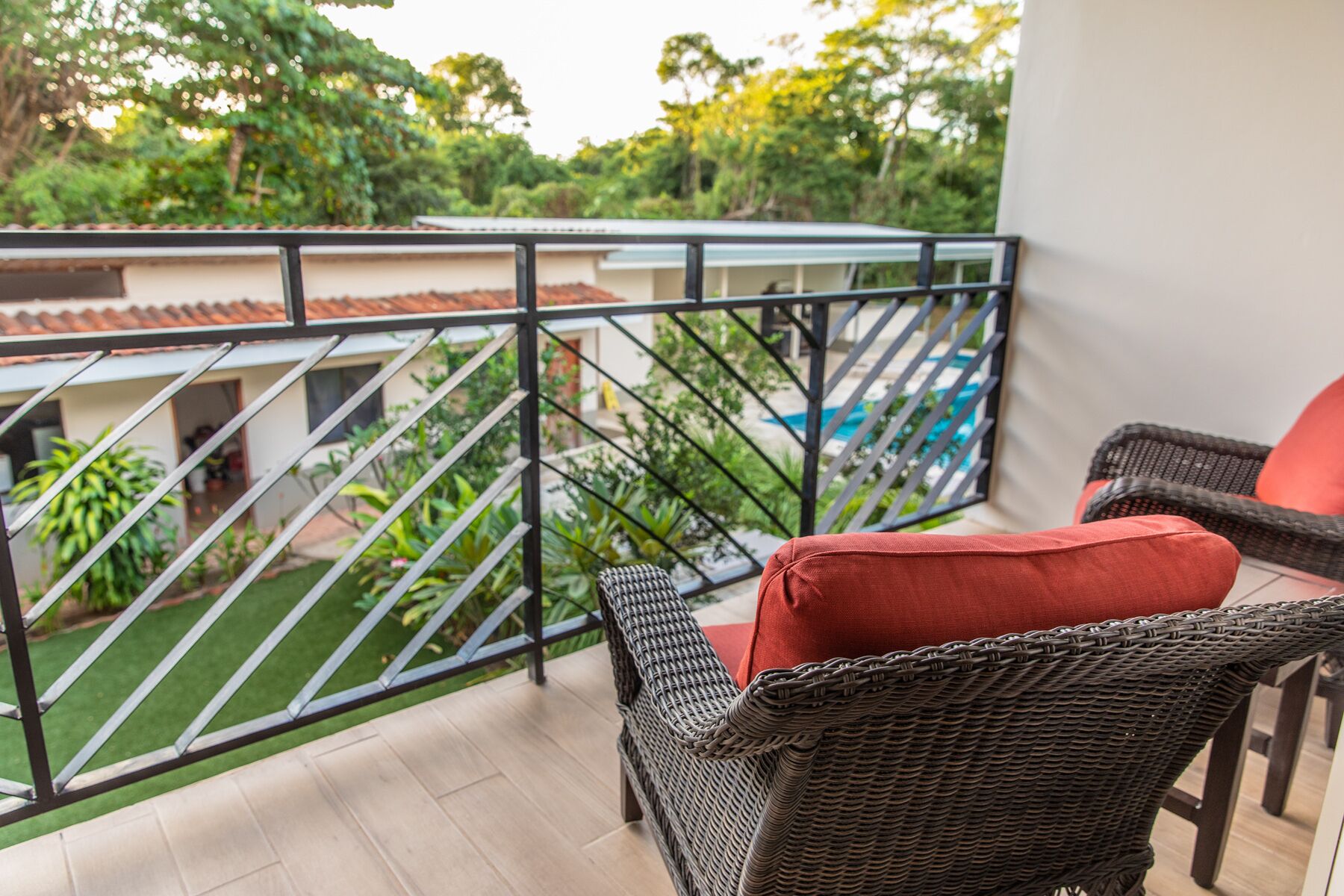 A balcony with wicker furniture and a view of a swimming pool and greenery.