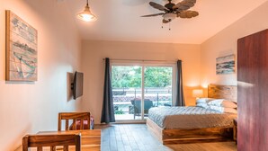 A bedroom with a bed, a desk, a chair, a ceiling fan, and a view of the outdoors. - Palm Beach Inn (Cabo Velas)