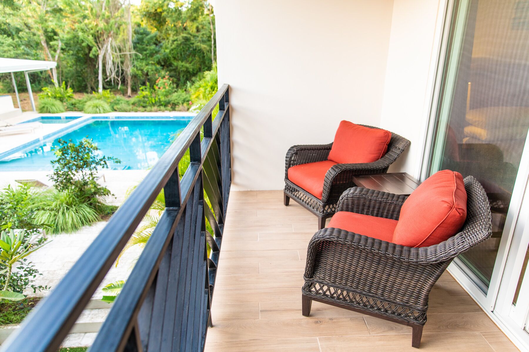 Un balcón con dos sillones de mimbre, una piscina y vistas a zonas verdes.