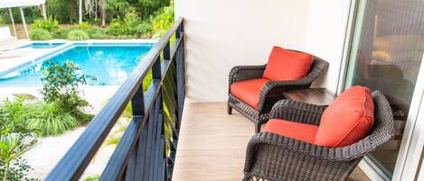 Un balcón con dos sillones de mimbre, una piscina y vistas a zonas verdes.