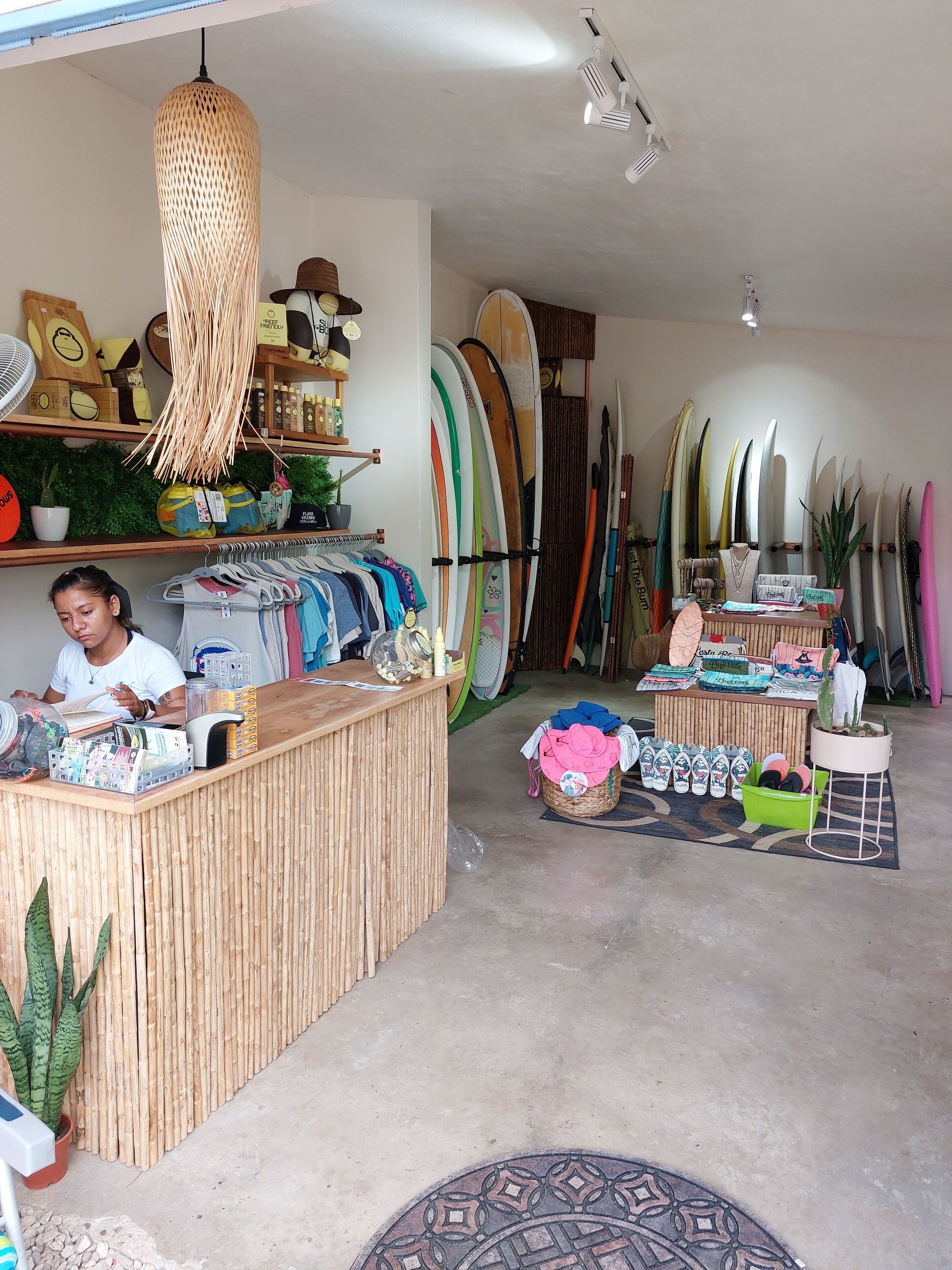 A surf shop with a wooden reception desk, surfboards, and various beach-related items.