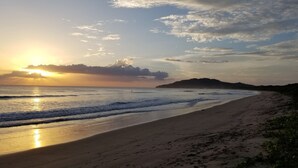 A beach with a sunset, waves, and a distant mountain. - Palm Beach Inn (Cabo Velas)