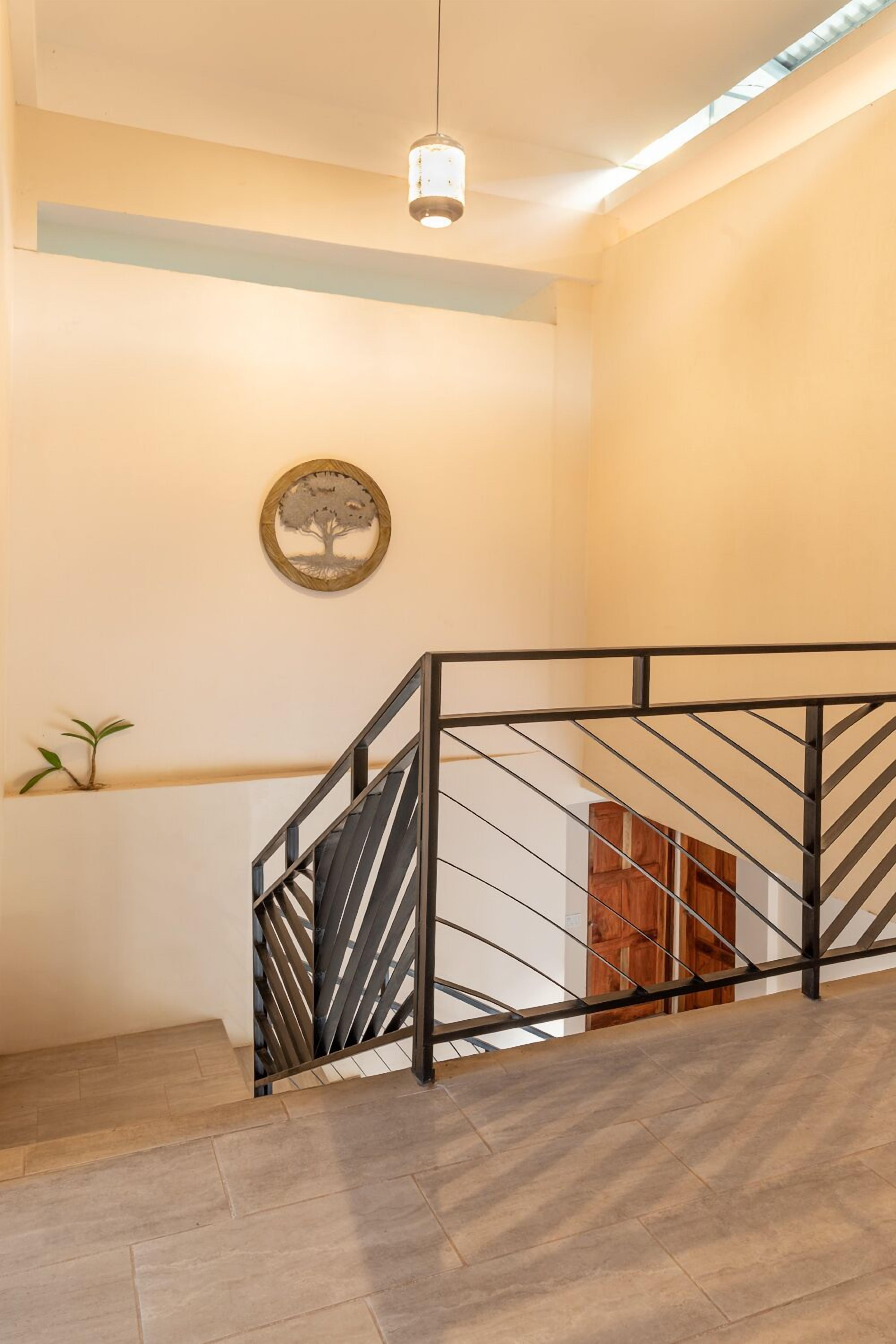 Una escalera con barandilla de metal negro, una puerta de madera al final y una lámpara fijada a la pared.