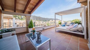 Eine Terrasse mit einer weißen Couch, einem Glastisch mit Flasche und Gläsern sowie Blumentöpfen.
