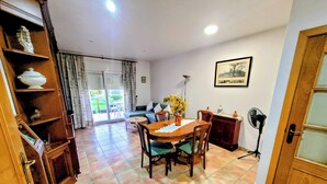 A dining area with a wooden table and chairs, a vase with yellow flowers, a bookshelf, a sofa, and a picture on the wall. - House in a quiet area with views of the old town of Pals (Pals)