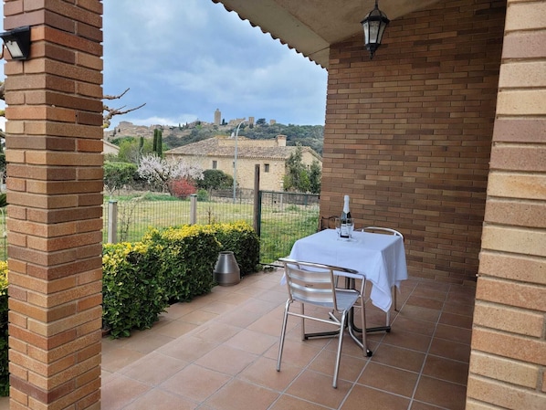 A patio with a table and chairs, a metal grill, and a view of a hill with buildings.