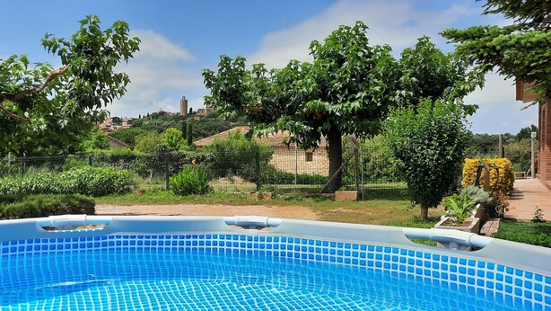 A swimming pool with a tiled edge, surrounded by greenery and a stone building in the background. - House in a quiet area with views of the old town of Pals (Pals)
