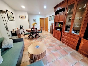A living room with a sofa, a dining table with chairs, a small round table, and wooden cabinets with glass doors.