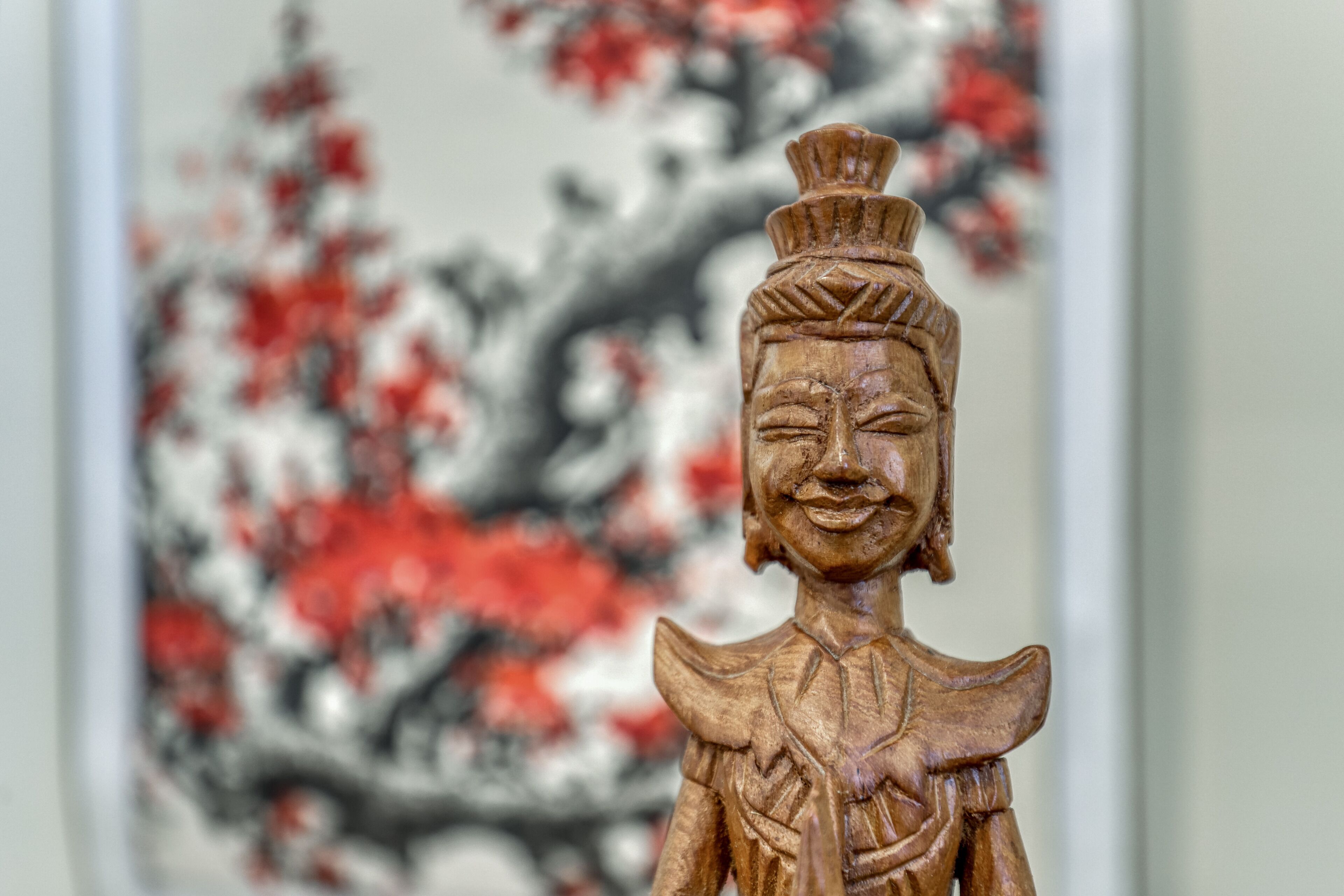 A wooden statue with intricate carvings, set against a blurred background of red and white foliage.
