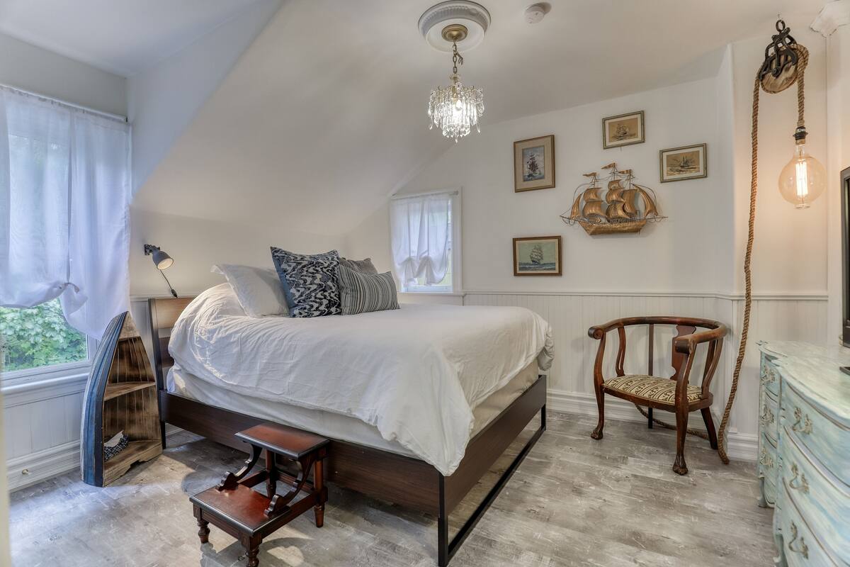 A bedroom with a large bed, a wooden chair, a dresser, and a chandelier.