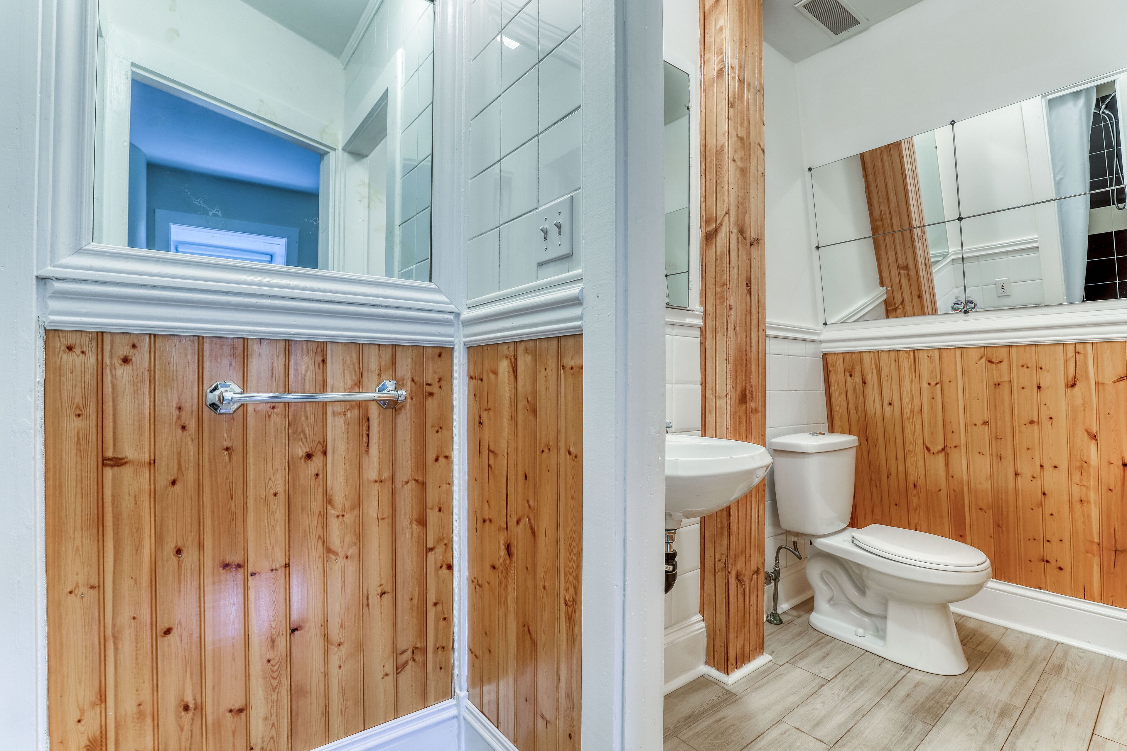 Un baño con paneles de madera, un lavabo blanco, un inodoro y un espejo grande.