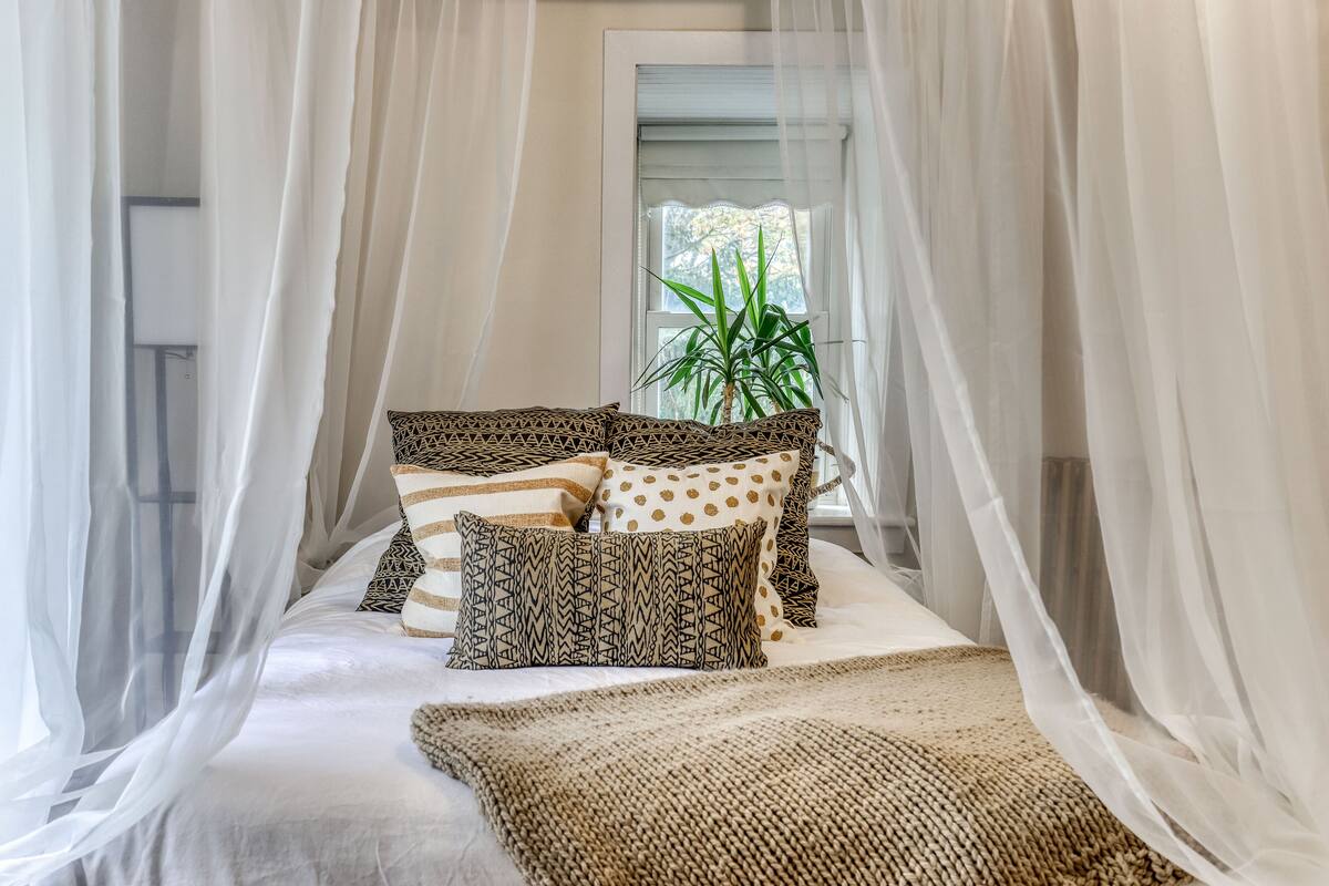 A bed with a canopy, patterned pillows, and a woven throw blanket.