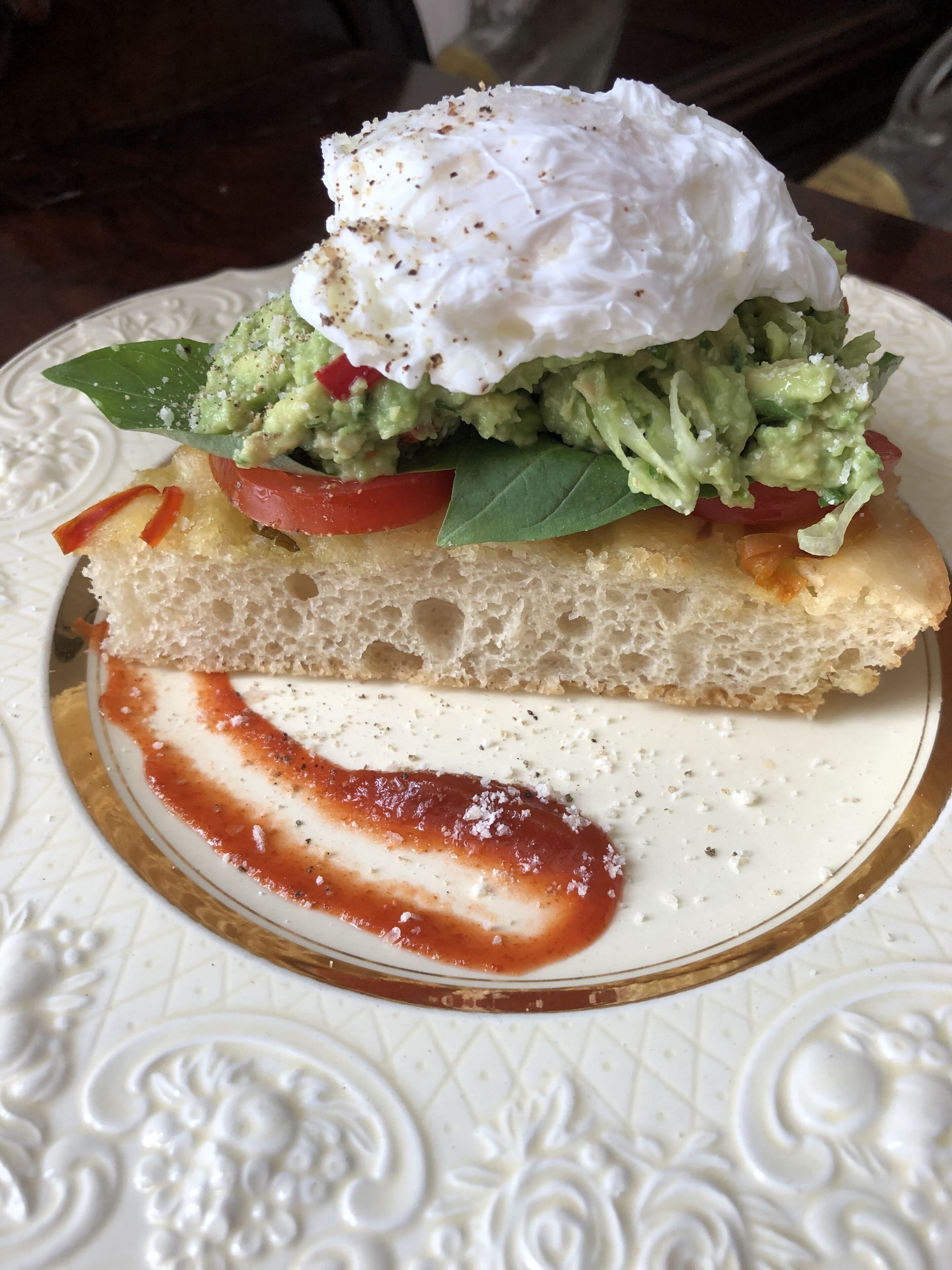 Sanduíche com abacate, tomate e ovo pochê numa fatia de pão, servido numa prato decorativo.