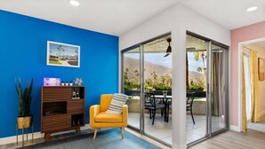 Ein modernes Wohnzimmer mit blauer Akzentwand, einer Holz-Unterhaltungseinrichtung, einem gelben Sessel und einer Glastür zu einer Außenpatio mit Tisch und Stühlen.