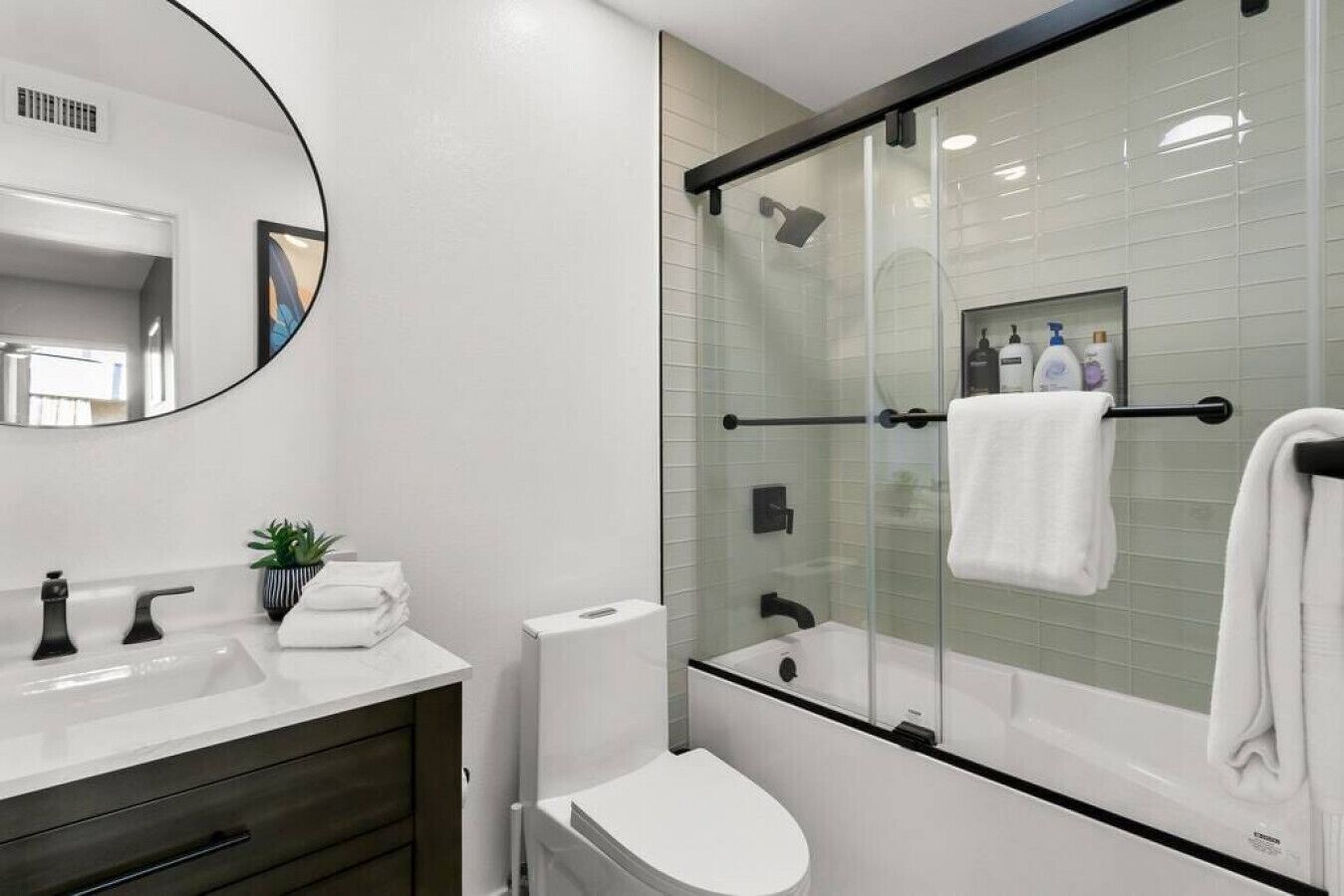 Une salle de bain moderne avec une douche à parois de verre, un lavabo blanc et un grand miroir.