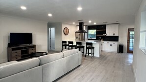 Un amplio salón con un sofá grande, un televisor de pantalla plana y una cocina al fondo.