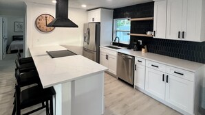 Una cocina moderna con armarios blancos, una isla central, electrodomésticos de acero inoxidable y un salpicadero negro.