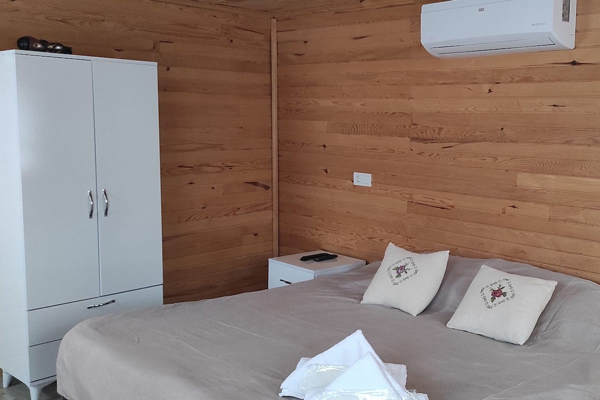 A bedroom with a bed, pillows, a wardrobe, a bedside table, and an air conditioner.