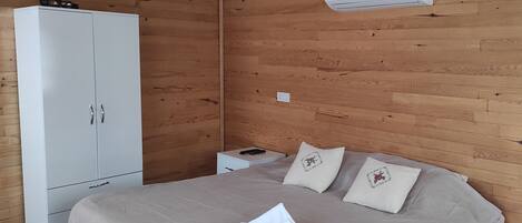 Un dormitorio con cama, almohadas, un armario, una mesita de noche y aire acondicionado.