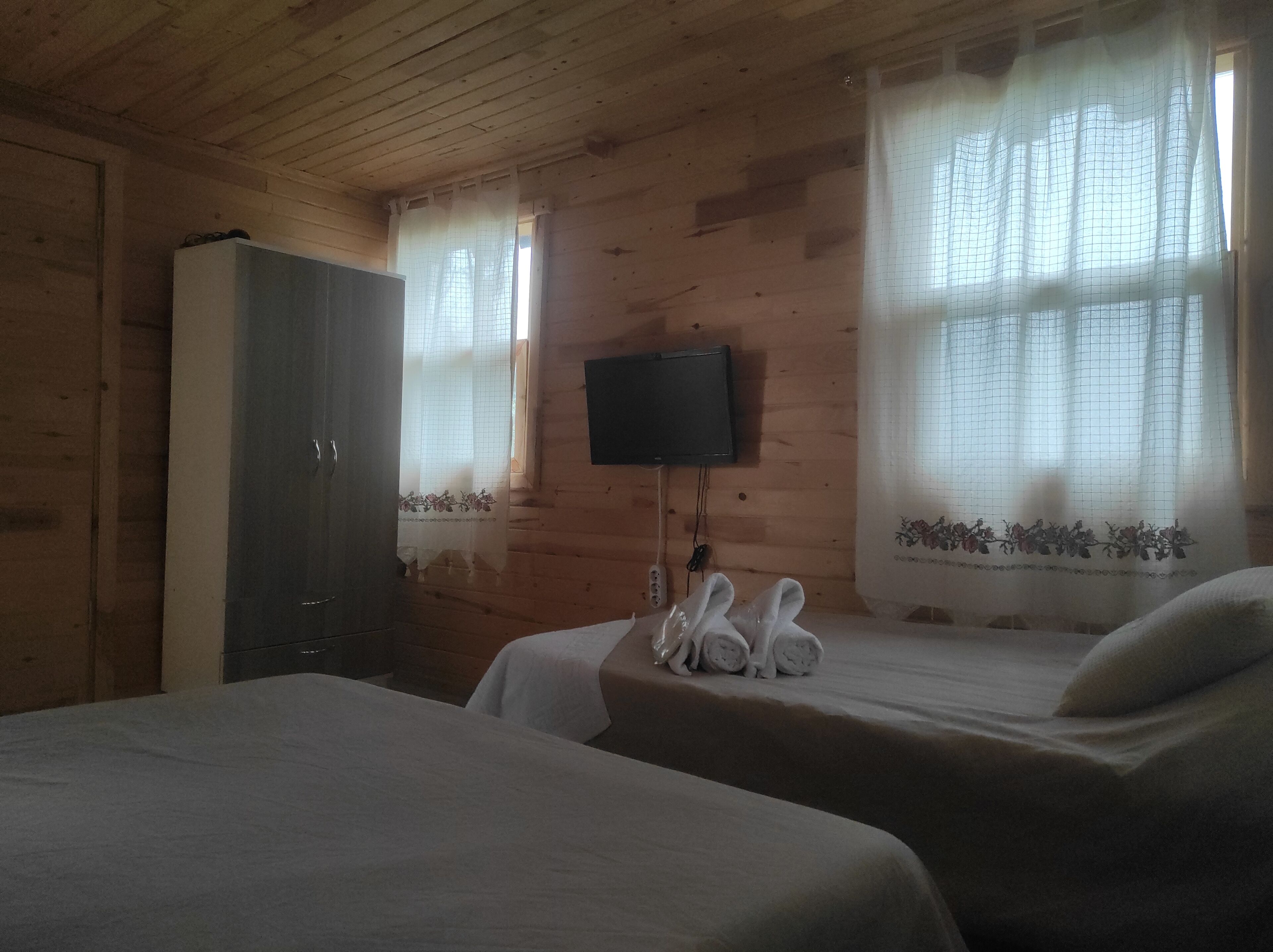 Habitación con paredes de madera, una cama, un televisor montado y una ventana con cortina.
