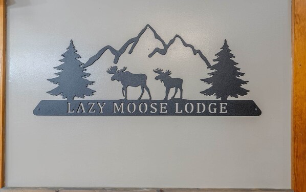 Un letrero muestra una montaña, árboles y un alce, con la leyenda 'LAZY MOOSE LODGE'.
