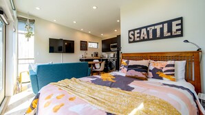 Une chambre d’hôtel moderne équipée d’un lit, d’un canapé, d’une télévision et d’un coin cuisine, avec un grand panneau portant l’inscription « SEATTLE » sur le mur.