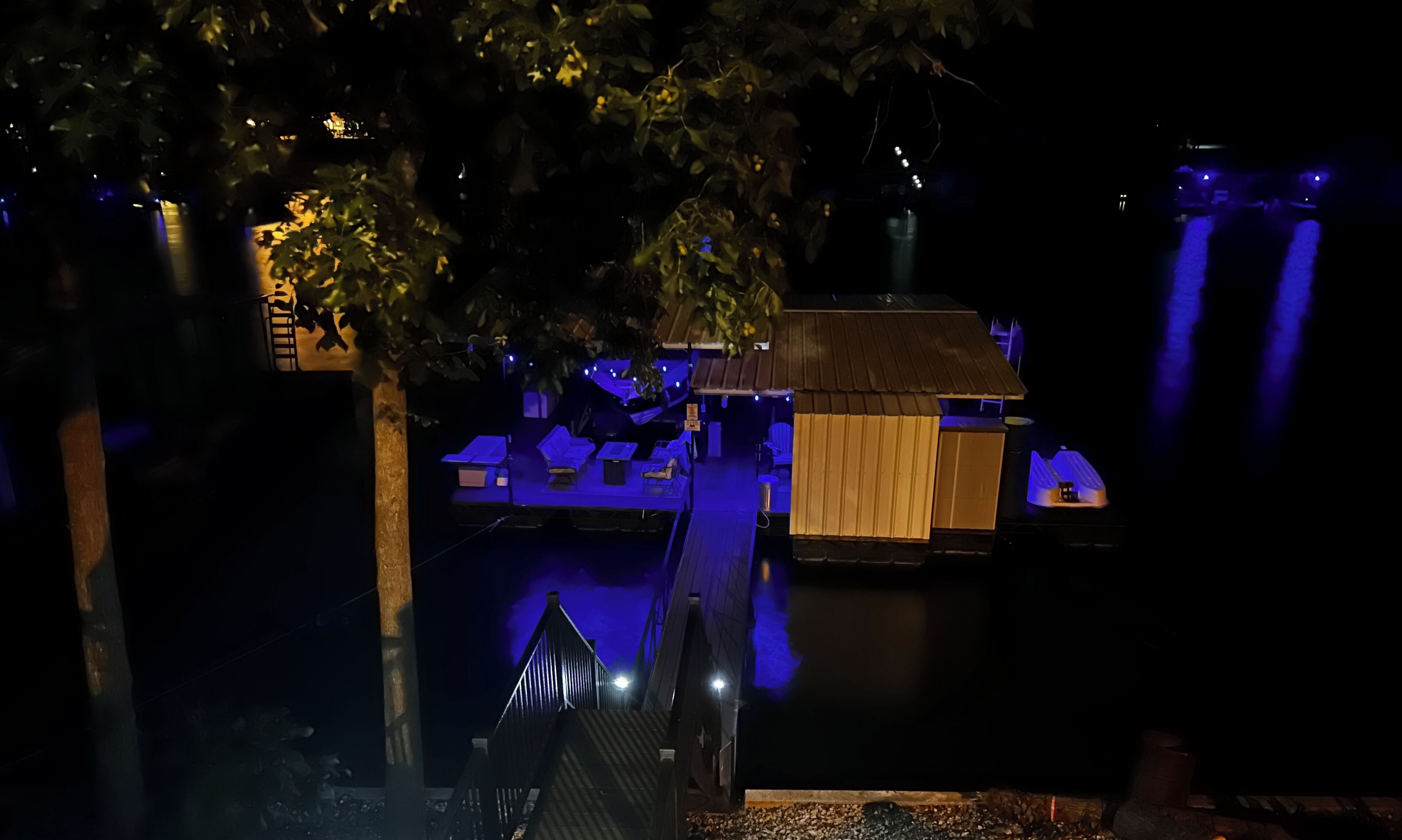 A nighttime view of a waterfront property with a dock, a small building with a thatched roof, and a row of lounge chairs.