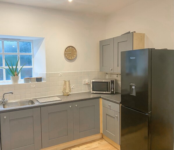 A kitchen with grey cabinets, a black refrigerator, a microwave, and a sink. - 4c Gaia Lane (Lichfield)