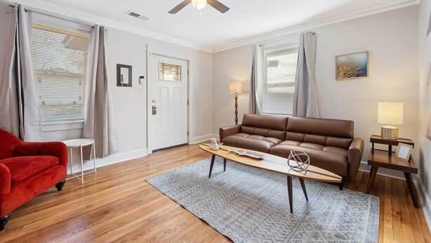A modern living room with a brown leather sofa, a red armchair, a wooden coffee table, and a ceiling fan. - 70's Boho 1 BR Near Zoo/Liberty Bowl/BBQ Fest!! (Memphis)