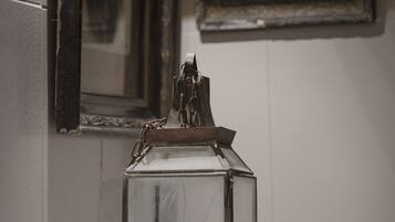 A glass lantern on a white surface with two framed pictures on the wall behind it.