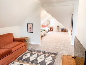 Relax in a spacious room with a high ceiling, featuring a sofa, patterned rug, and artwork on the wall.