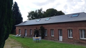 A brick building with a sloped roof, multiple windows, and a small patio area with a table and chairs. - 3 Bedroom Private vacation home in ROSAY SUR LIEURE (ROSAY SUR LIEURE)