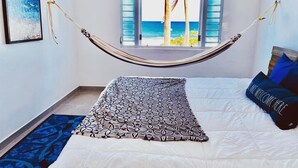 A bedroom with a hammock tied between the window and bed, a patterned throw blanket, and a pillow with a message. - breathtaking sea view Beach FRONT very PRIVATE and quiet SOLAR POWERED (Arecibo)