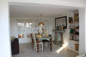 Un coin repas comprenant une table en bois, des chaises, une suspension et une bibliothèque avec des livres et des objets décoratifs.