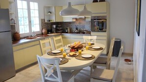 A modern kitchen with a round dining table, white chairs, and a breakfast setting. - Große Villa für max. 12 Personen mit Privatpool und schönem Garten, Meerblick (La Croix Valmer)