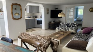 A modern living room with a sofa, a coffee table, and a dining table. There is a kitchen area with cabinets and a television. - Große Villa für max. 12 Personen mit Privatpool und schönem Garten, Meerblick (La Croix Valmer)