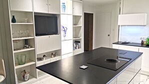 Eine moderne Küche mit weißen Schränken, einer zentralen Kochinsel mit eingebautem Herd und einem Flachbildfernseher, der über der Insel angebracht ist.