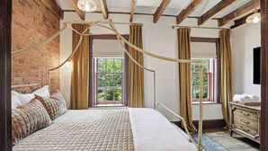 Ein Schlafzimmer mit Himmelbett, Backsteinwand und einem großen Fenster mit Vorhängen.