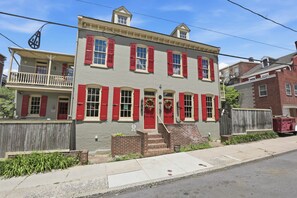 A two-story building with a balcony, red shutters, and a front door.