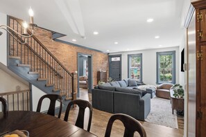 A modern living room with a staircase, a dining area, and a large gray sectional sofa.