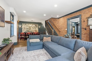 A living room with a sectional sofa, a dining area with a table and chairs, a staircase, and a large mirror. - Historic 8 Bedroom Luxury Retreat - Hot Tub - Sleeps 20+ - Walk Downtown (Lancaster)