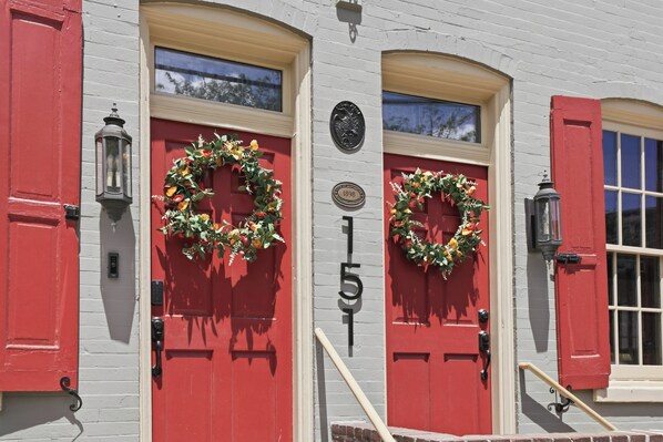 A building with two red doors, each adorned with a wreath, and a number plaque reading '151'.