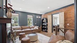 Ein Wohnzimmer mit Ledersofa, Poufs, Kamin, Bücherregal und einer Ziegelwand.