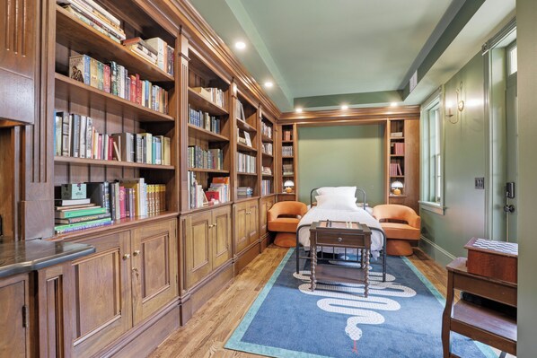 A library with bookshelves, a bed, a desk, and a chessboard.