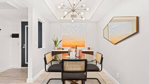 A modern dining area with a round table, four chairs, a central light fixture, and a large framed picture on the wall. - Newly renovated, vibrant and chic Biltmore condo (Palm Springs)