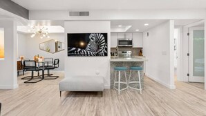 A modern kitchen with a microwave, stove, and bar stools. There is a dining area with a table and chairs, and a large zebra print artwork on the wall. - Newly renovated, vibrant and chic Biltmore condo (Palm Springs)