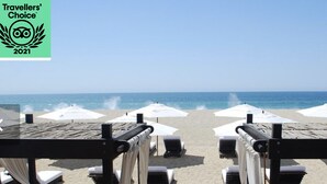 Ein Strand mit Liegestühlen und Sonnenschirmen, ein klarer Himmel und das Meer im Hintergrund.