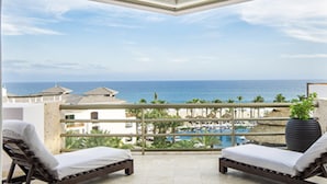 Ein Balkon mit zwei Liegestühlen, einem Blumentopf und Blick auf das Meer und die Hotelgebäude.