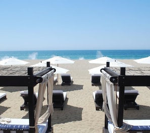 Une plage bordée de rangées de transats et de parasols, un ciel dégagé et l’océan en toile de fond.